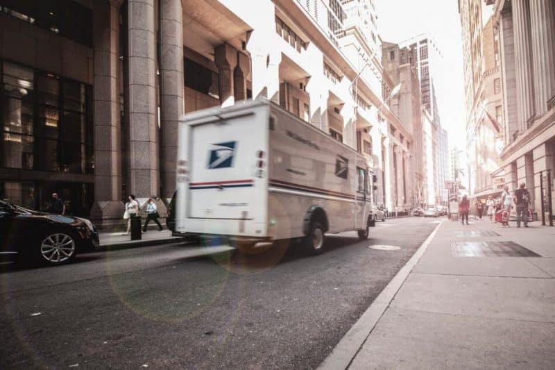 cara mencari supplier yang baik dan terpercaya, kendaraan putih pengangkut barang/ paket sedang mengantar pesanan pelanggan dengan truk, melintas dengan cepat di jalan raya