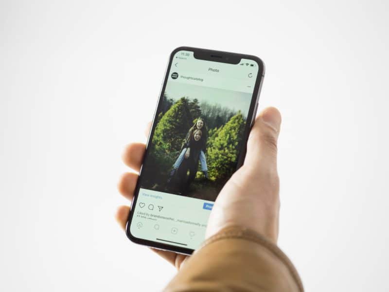 tangan sedang menggenggam handphone android hitam yang terbuka beranda aplikasi instagram, cara menggunakan instagram versi terbaru bagi pemula