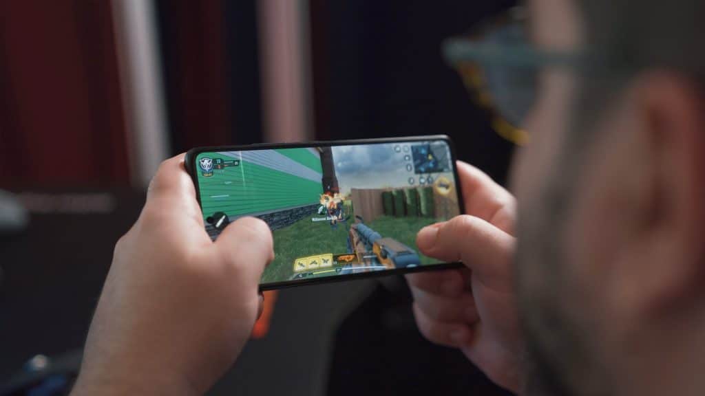 Seorang laki-laki/pria sedang bermain game smartphone android tembak tembakan, close up dari belakang