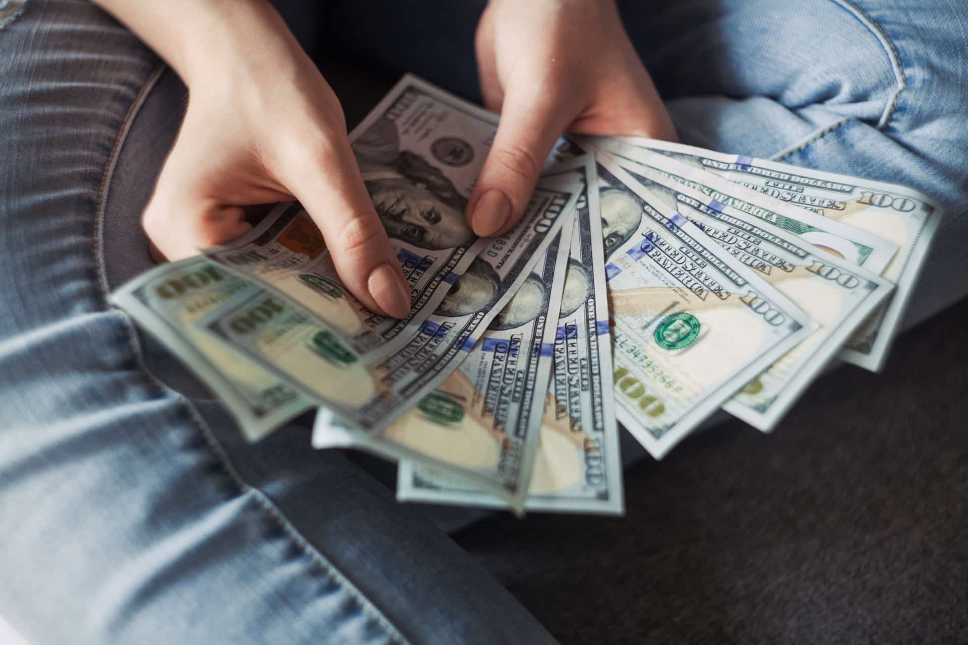 tangan perempuan sedang memegang beberapa lembar uang dolar